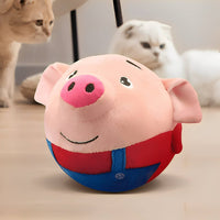 Der rosa Schweinchen-Plüschball mit blauer Latzhose steht auf dem Boden, im Hintergrund schauen zwei Katzen zu. 3